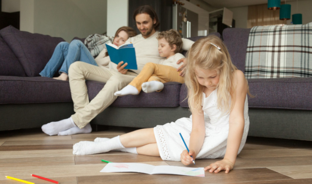 Mama, tata i syn czytają książkę na kanapie, a córka bawi się na podłodze - jaka optymalna temperatura w domu?