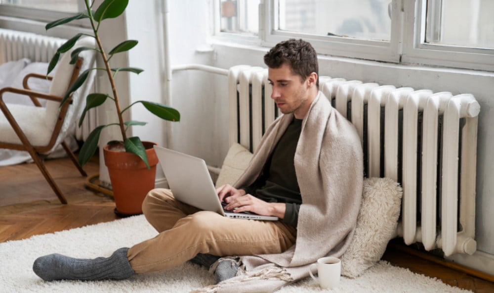Mężczyzna z laptopem siedzący przy grzejniku i analizujący źródła ciepła